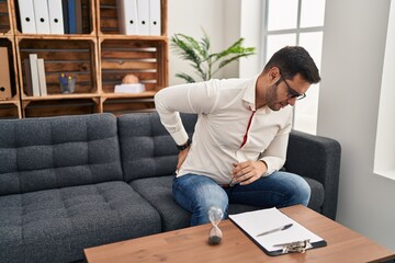 Young hispanic man with beard working at consultation office suffering of backache, touching back with hand, muscular pain