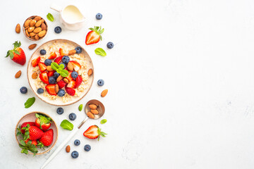 Oatmeal porrige with fresh berries and nuts on white background. Healthy breakfast, top view with copy space.