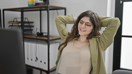 Young beautiful hispanic woman business worker sitting on table relaxing with hands on head at office