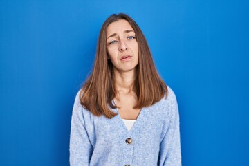 Fototapeta premium Young woman standing over blue background looking sleepy and tired, exhausted for fatigue and hangover, lazy eyes in the morning.