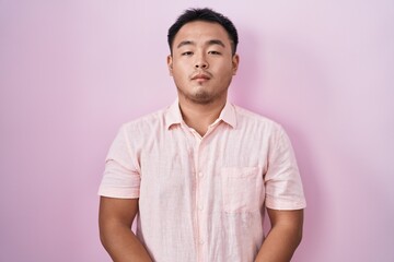 Chinese young man standing over pink background relaxed with serious expression on face. simple and natural looking at the camera.