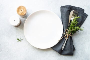 Fototapeta na wymiar White plate, shaker and cutlery on stone table. Table setting, flat lay image.