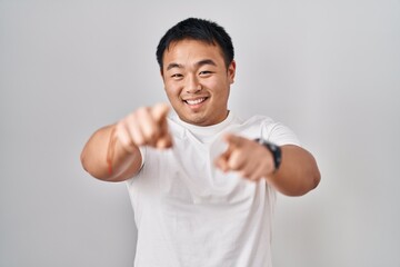 Young chinese man standing over white background pointing to you and the camera with fingers, smiling positive and cheerful