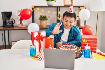 Young chinese man celebrating birthday with cake doing video call looking positive and happy standing and smiling with a confident smile showing teeth