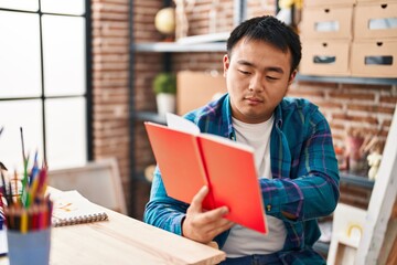 Naklejka premium Young chinese man artist reading book at art studio