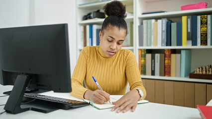 Young african american woman student using computer taking notes at the library