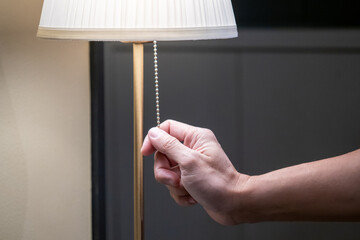 Saving electricity energy concept. Male hand pulling light switch chain on white lamp in the...