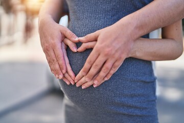 Man and woman couple hugging each other doing heart gesture on belly at street