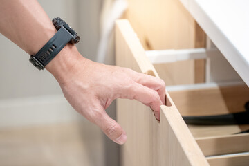 Male hand pulling and opening drawer on wooden cabinet in furniture store.