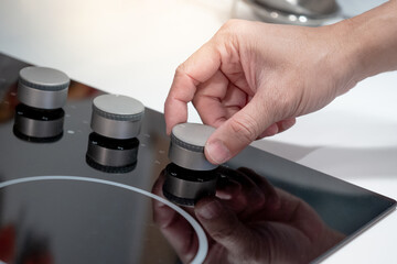Male hand turning knob on electric hob or electric stove in kitchen showroom. Cooking appliance in...