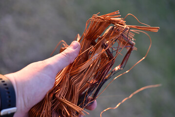 A bundle of copper wire in his hand. Copper scrap. Shiny red copper wire.