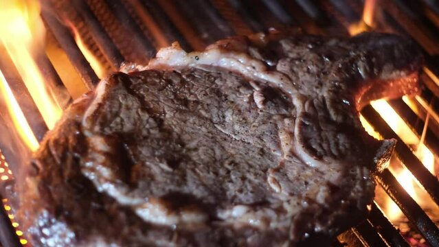 Beef steak on grill with fire flame. Meat beef steak on grill close-up. Barbecue grill. Raw beef steak grilling. Barbecued meat and fire. Barbecued beef on smoking and flaming grill. Bbq culinary.