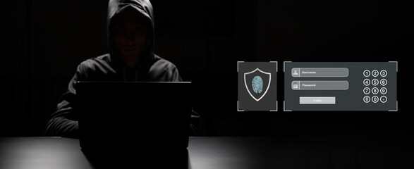Professional hacker with laptop and mobile phone sitting at table on dark background