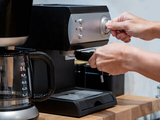 Male barista hand holding coffee holder turning knob on coffee machine on countertop.