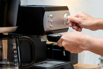 Male barista hand holding coffee holder turning knob on coffee machine on countertop.