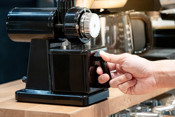 Buying coffee maker equipment. Male hand holding black coffee grinder machine in barista tool shop.