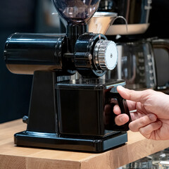 Buying coffee maker equipment. Male hand holding black coffee grinder machine in barista tool shop.