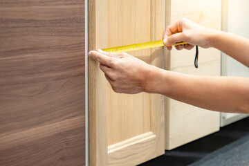 Male hand using tape measure on wooden cabinet panel display in furniture store. Buying furniture for home interior design
