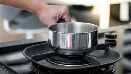 Shopping kitchen utensils concept. Male hand holding stainless steel saucepan on gas stove in kitchenware showroom store. Buying cookware for the domestic kitchen at home.