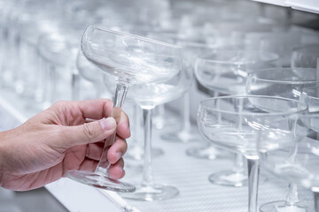 Customer hand picking empty champagne coupe glasses from product rack. Buying glassware in home decoration store - obrazy, fototapety, plakaty