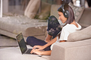 Headphones, typing and woman with laptop on home sofa listening to music, audio or streaming movies. Happy female student relax on couch to listen to podcast or research to learn language on internet