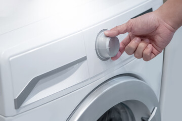 Hand turning knob setting program on automatic washing machine in laundry.
