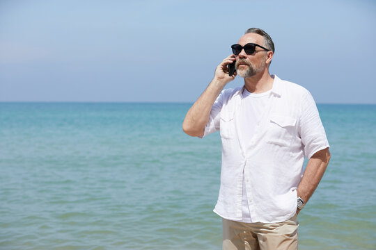 senior man talking by smartphone on the beach