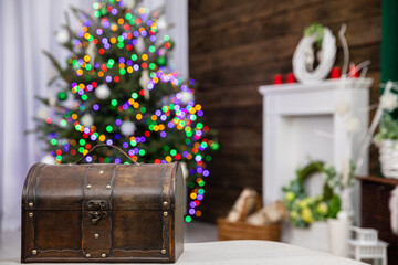 A brown old box in the foreground and a Christmas tree with Christmas lights in the background.
