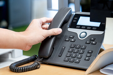 Call center and customer support. Operator hand trying to response customer call by using landline VoIP phone on help desk in the office.