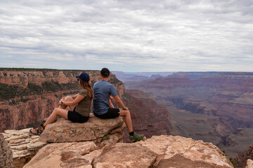 Naklejka na ściany i meble Loving couple sitting on rock with scenic view from Skeleton Point on South Kaibab hiking trail at South Rim, Grand Canyon National Park, Arizona, USA. Colorado River weaving through rugged terrain