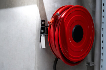 Red fire hose reel installed on the concrete wall in the factory or warehouse. Fire extinguisher equipment