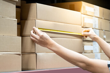 Male worker hands using tape measure on carton box in warehouse. Checking dimensions for goods...