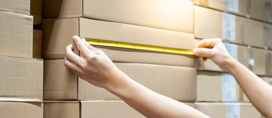 Male worker hands using tape measure on carton box in warehouse. Checking dimensions for goods...