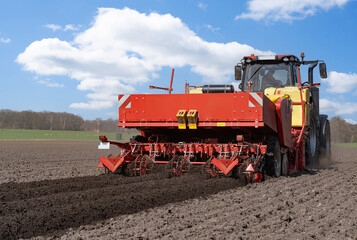 Obraz premium Großer, roter Traktor mit einer Karoffelpflanzmaschine im Frühjahr auf dem Kartoffelfeld im Einsatz. 