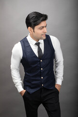 Studio shot of cheerful, young, handsome Indian business man in formal wear against grey background. Male model. Fashion Portrait.