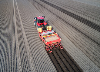 Drohnenfoto - Traktor mit Kartoffellegemaschine beim legen von Saatkartoffeln, die Kartoffeldämme...