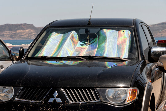 Crete, Greece, EU. 2023. Sunshade inside the windscreen of a dirty black car, Dead flies stuck to bodywork.