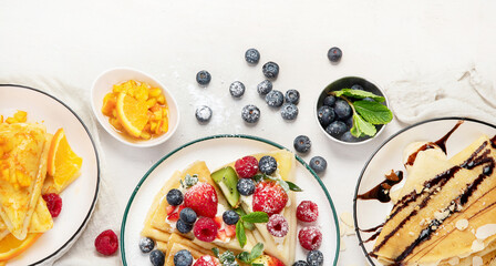 Sweet crepes assortment with berries chocolate on gray background. Homemade food concept. Top view, flat lay
