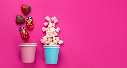 Paper cups with different candies on pink background.