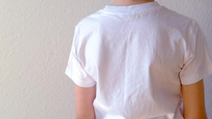 back of boy, child 8-10 years old in a white t-shirt grabbed a sore spot, curved spine, wrong posture, symbol of pain in spine, concept of osteochondrosis, scoliosis, back pain, intervertebral hernia