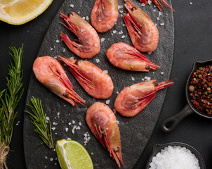 Boiled shrimp on a board, lemon slices, spices on a black background, top view