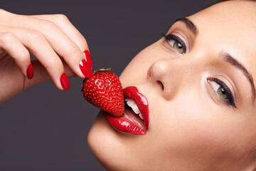 Makeup, portrait and woman with a strawberry in a studio with red nails and lipstick cosmetics. Health, wellness and closeup of a female model eating fruit for nutrition isolated by a gray background