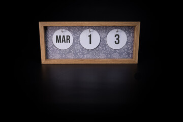 A wooden calendar block showing the date March 13th on a dark black background, save the date or date of event concept.