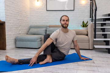 Fototapeta premium Man practicing yoga at home on floor on yoga mat stretching body.