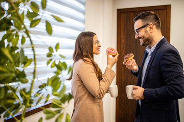 Two businesspeople having conversation inside company office and eating donuts.