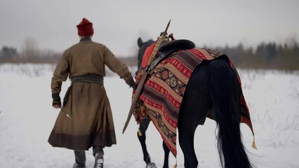 horseman in historical gown of 12 century leading black horse, back view, history reconstruction