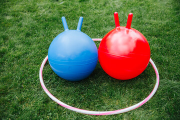 childhood, leisure and toys concept - bouncing balls or hoppers and hula hoop on grass