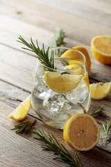 Gin tonic with ice, rosemary, and lemon slices on an old wooden table.