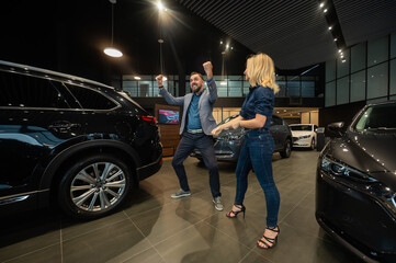 Naklejka na ściany i meble Happy married couple celebrating buying a car in a car showroom.