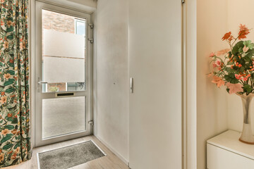 a flower in a vase on the wall next to an open door with a window behind it and some flowers